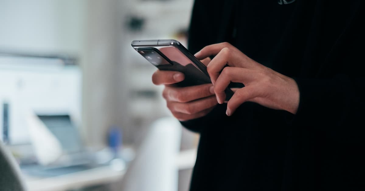 A person tapping a reply on their smartphone with a laptop open in the background